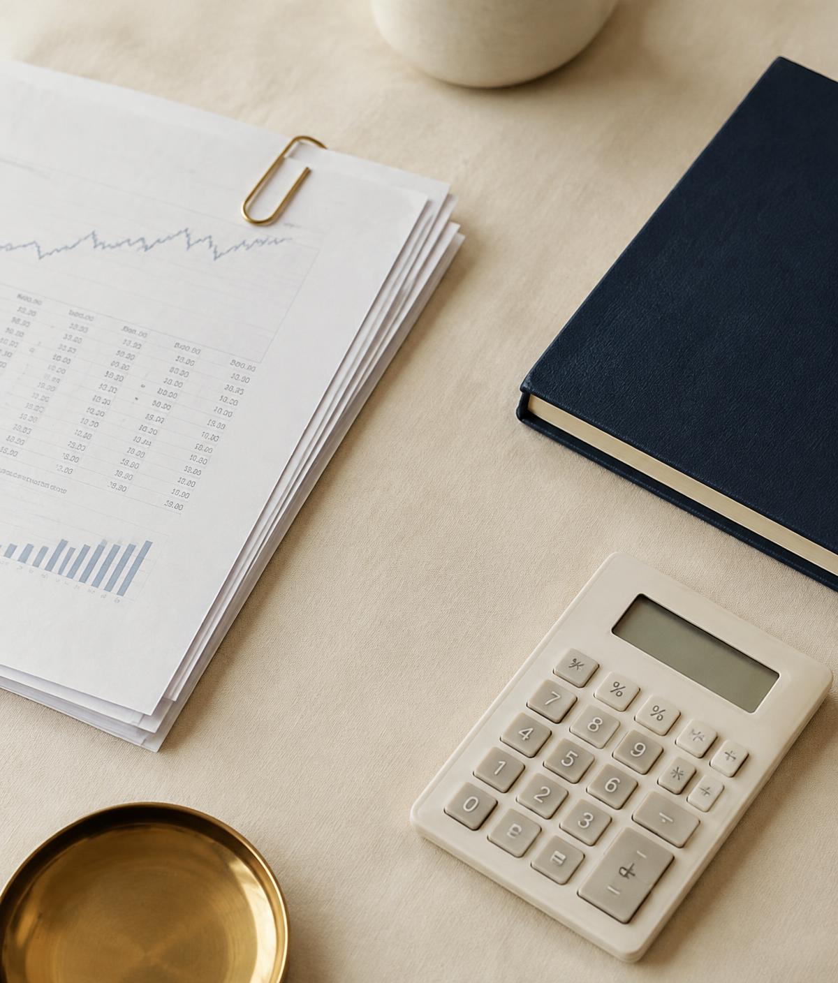Neatly organized financial documents, a calculator, and a navy notebook on a linen desk